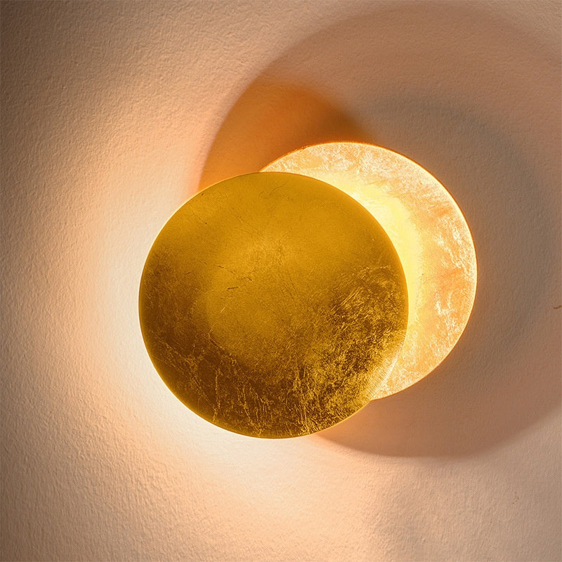 Decorative wall sconce with a gold and beige finish on a textured wall.