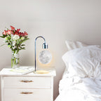 Decorative lamp with moon design on a nightstand next to a bed with white bedding.