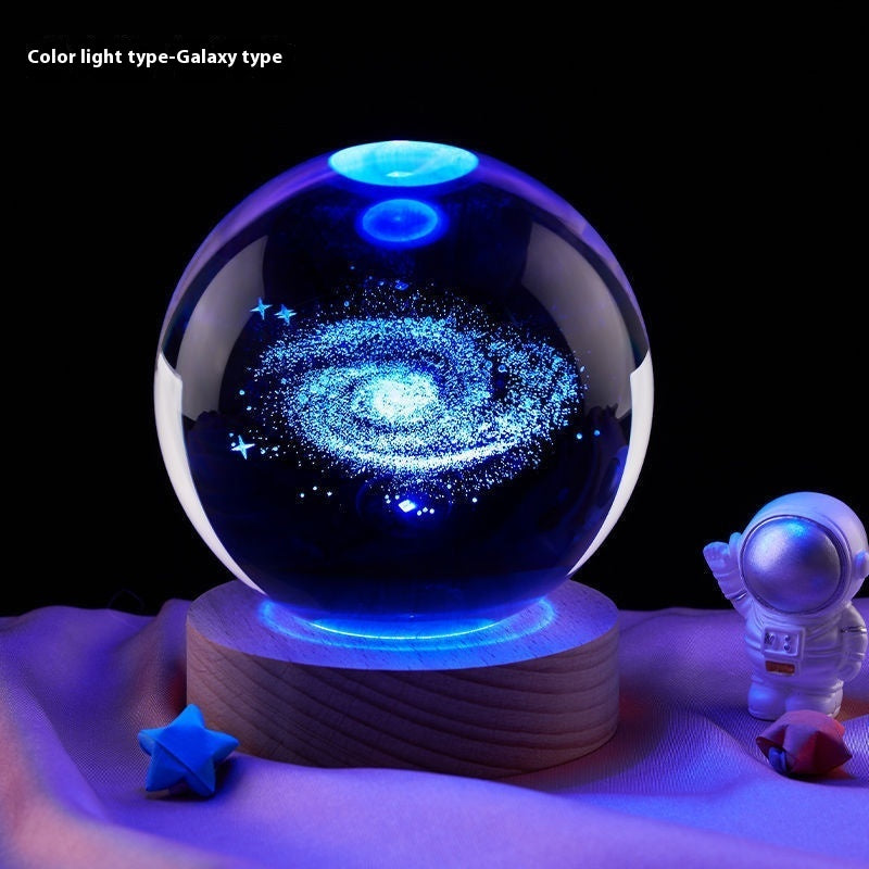 Glass ball with galaxy design on a wooden base, surrounded by space-themed decor.