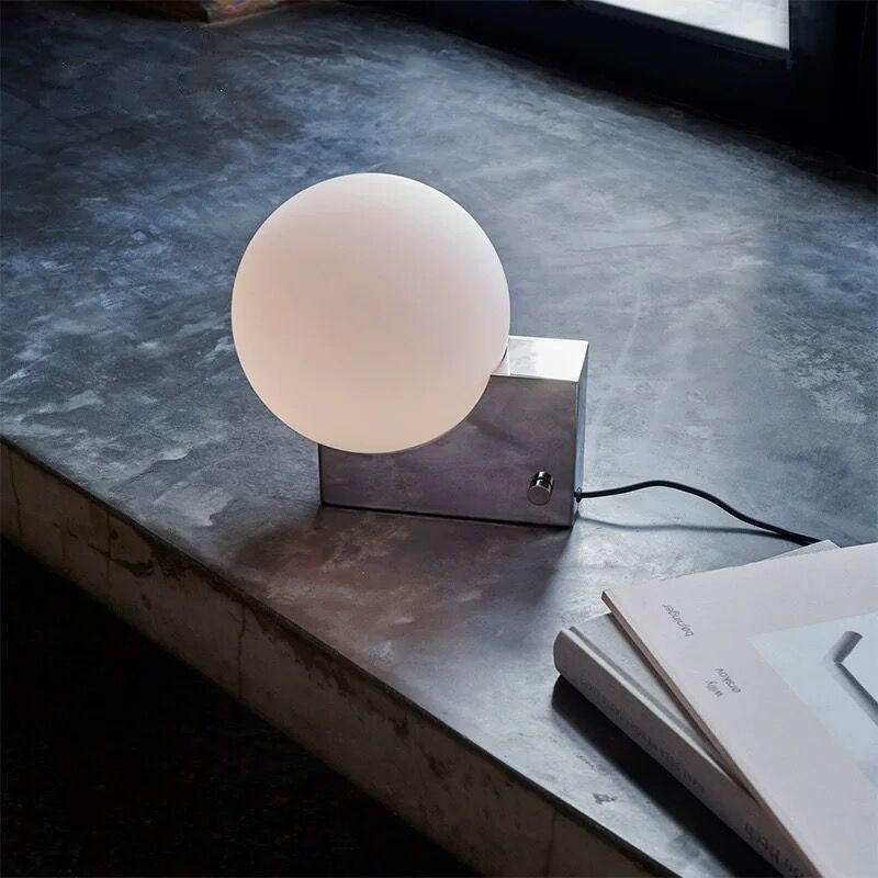 Modern table lamp with a spherical glass shade on a concrete surface.