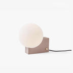 Modern wall-mounted lamp with a round white shade on a light beige base against a white background.