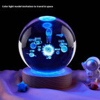 Decorative crystal ball with space-themed design on a wooden base, surrounded by small astronaut figures and celestial bodies.