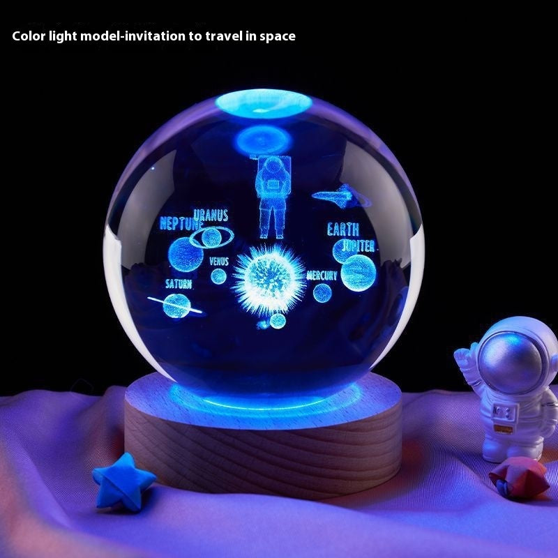 Decorative crystal ball with space-themed design on a wooden base, surrounded by small astronaut figures and celestial bodies.
