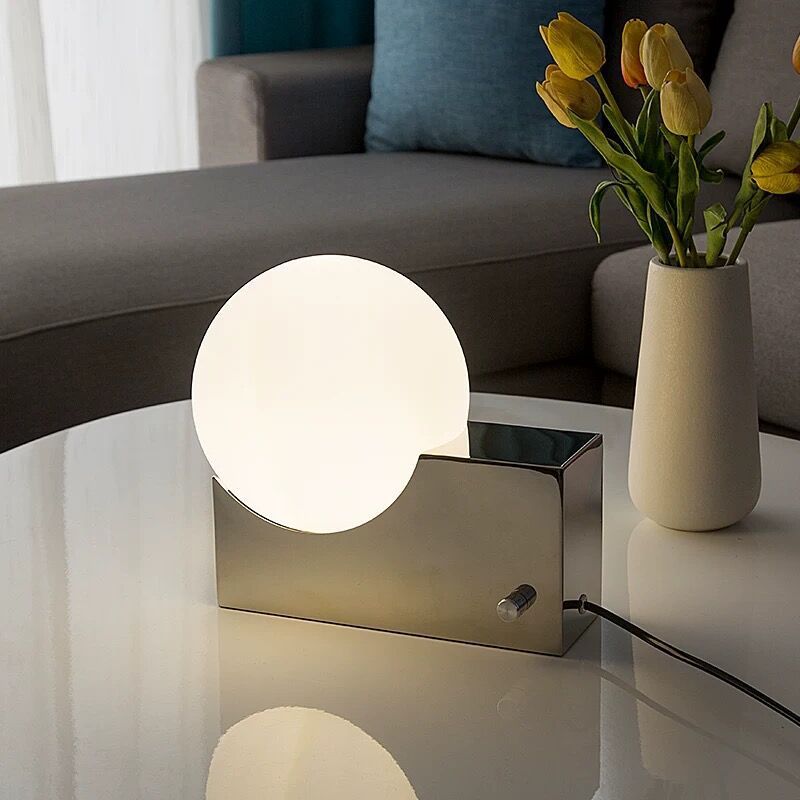 Modern table lamp on a reflective surface with a vase of tulips in the background