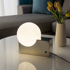 Modern table lamp on a reflective surface with a vase of tulips in the background