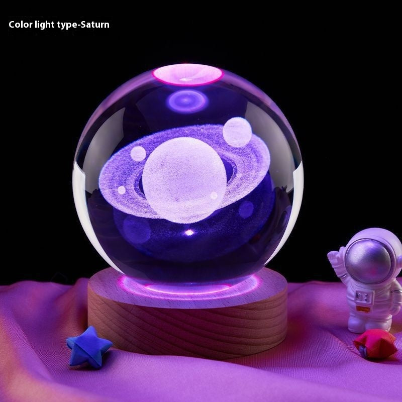 Glass ball with Saturn design on a wooden base, surrounded by space-themed decorations.